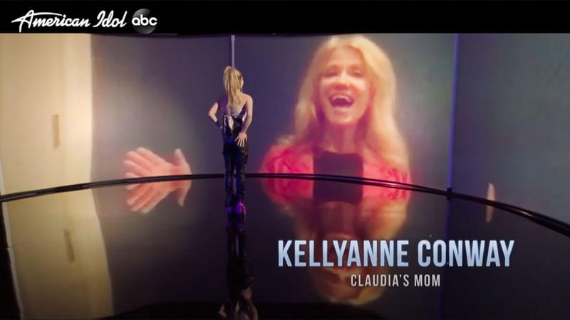 Kellyanne Conway heijastetaan suurelle valkokankaalle hymyillen, kun Claudia seisoo sen edessä.